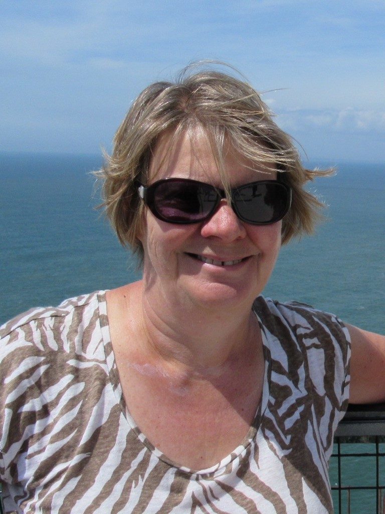 Jean Waller Jean Waller smiling with sunglasses on in front of an ocean